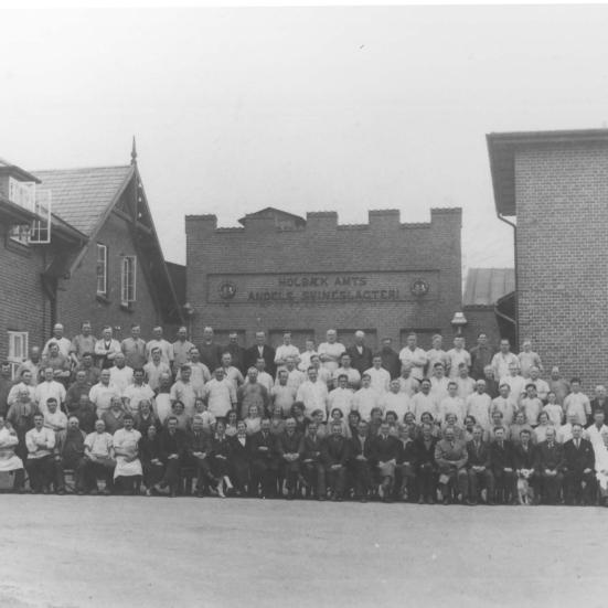 Sort-hvid foto af en stor flok medarbejdere opstillet uden for slagteriets bygninger.