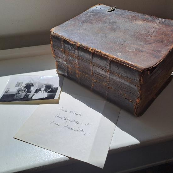 Farvefoto af en tyk skindindbundet bog samt et foto og en konvolut.