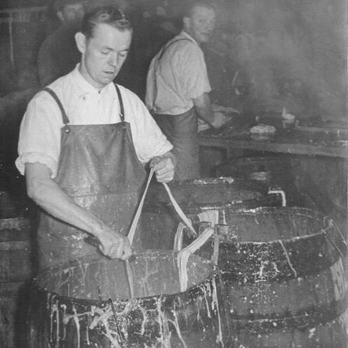 Sort-hvid foto af en mand, der arbejder med tarme ved en tønde.