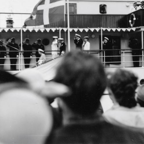 Sort-hvid foto af kongeskibet med kongeparret, der er på vej i land ad gangbroen. Menneskemængde på kajen.