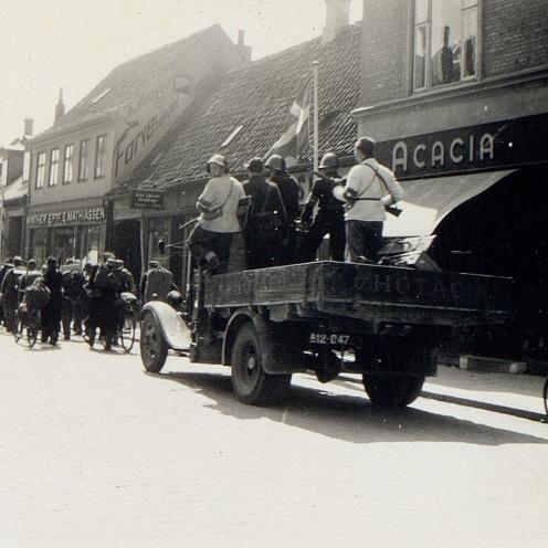 Sort-hvid foto af en lastbil med modstandsfolk bag en lang række tyske soldater.