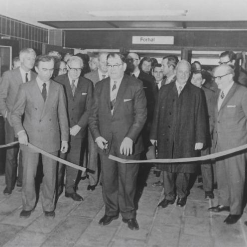 Sort-hvid foto af mand, der klipper snor med en flok tilskuere, der ser til.