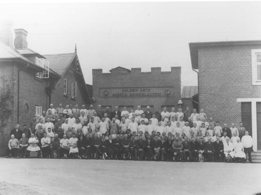 Sort-hvid foto af en stor flok medarbejdere opstillet uden for slagteriets bygninger.
