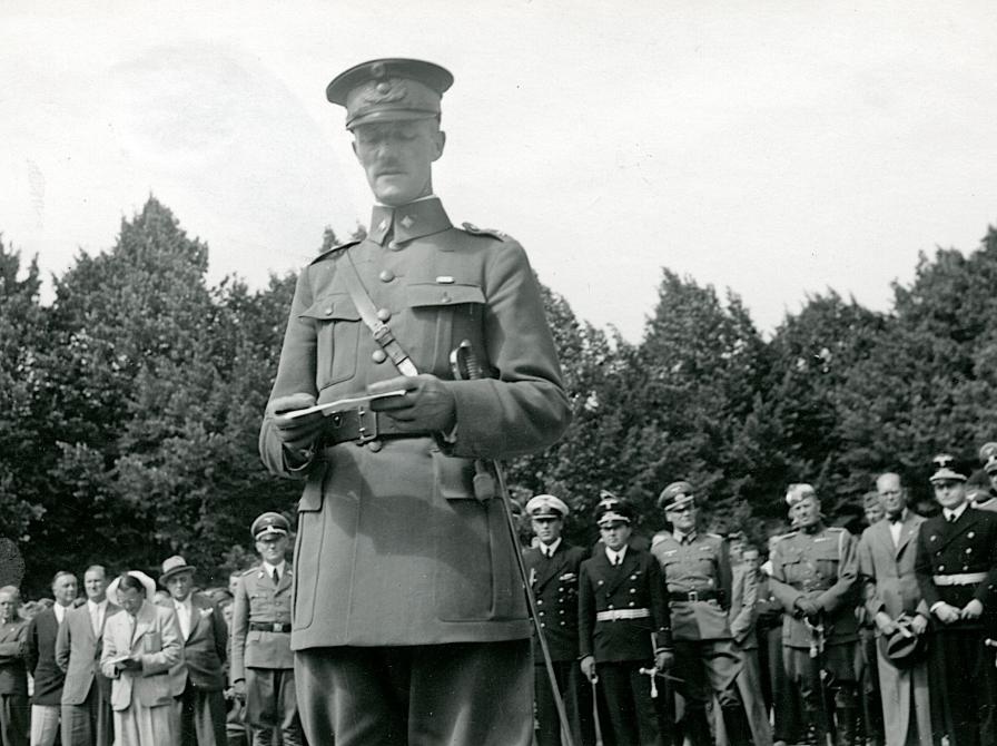 Sort-hvid foto af uniformeret mand der læser op af et stykke papir.