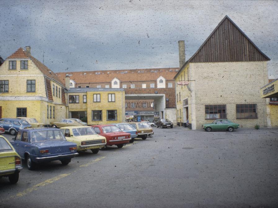 Farvefoto af gårdmiljø med en række parkerede biler.