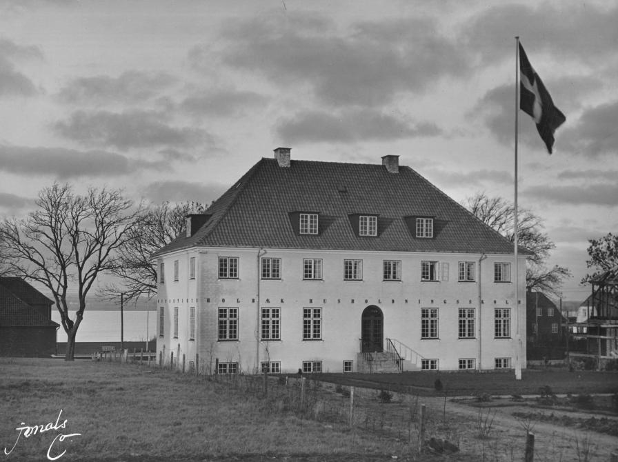Sort-hvid foto af en toetages bygning med Holbæk Fjord i baggrunden.